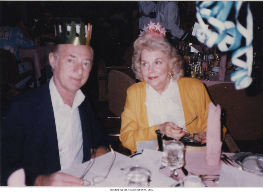3 1/2 x 5 inch photograph; Jane and Leonard Feather wearing paper crowns, in a restaurant