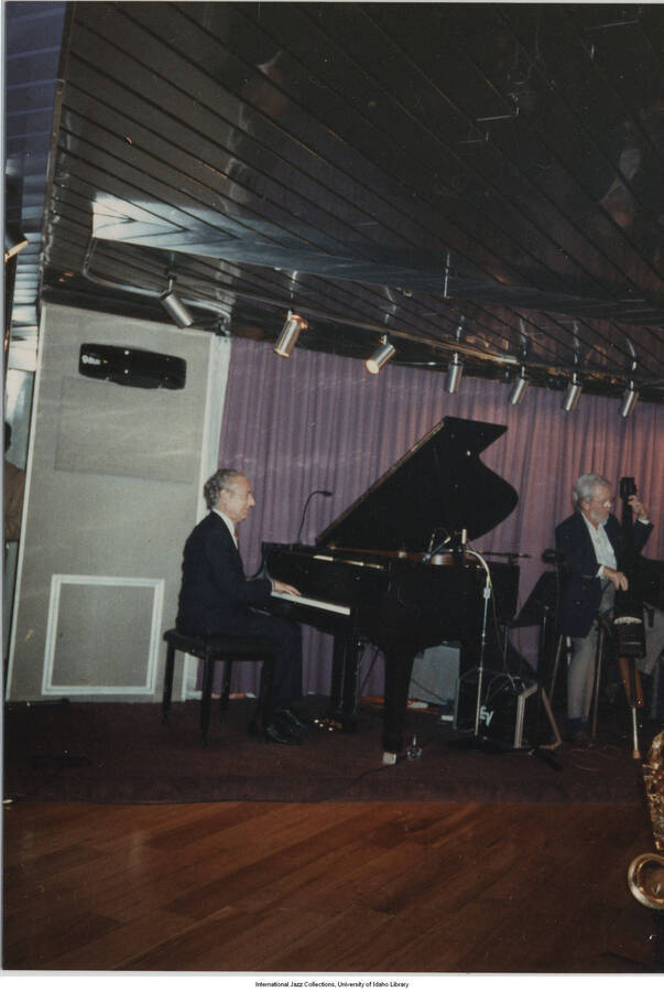 5 x 3 1/2 inch photograph; Leonard Feather playing the piano along with unidentified musicians