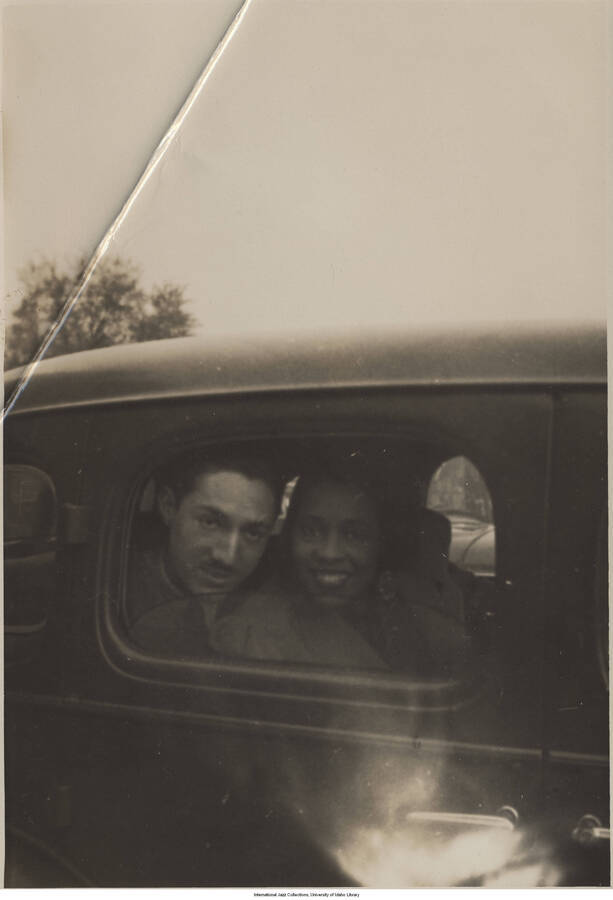 6 3/4 x 4 3/4 inch photograph; Leonard Feather and an unidentified woman inside a car, looking through the window