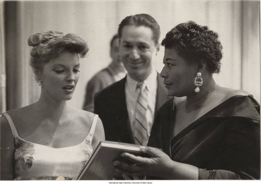7 1/2 x 10 inch photograph; Label on the back of the photograph reads: Julie London presenting Ella Fitzgerald with her copy of the Encyclopedia Yearbook of Jazz for winning the poll for best female singer