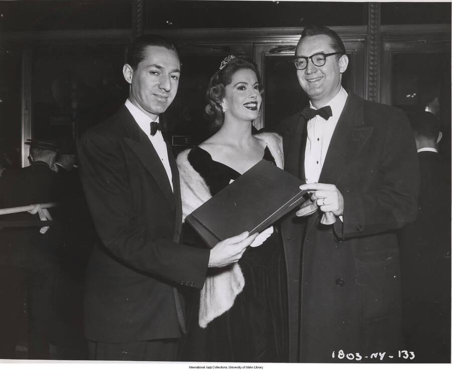 8x10 inch photograph. Leonard Feather with Jayne Meadows and Steve Allen. Leonard Feather is presenting a  portfolio to Steve Allen, that reads on the cover: To Steve Allen