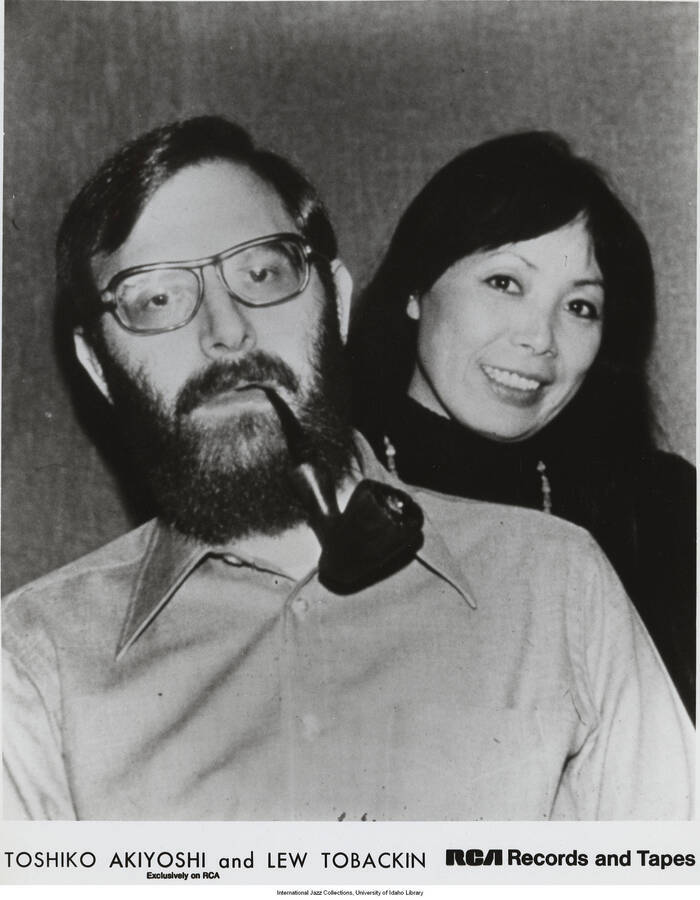 10 x 8 inch photograph; Toshiko Akiyoshi and Lew Tabackin. Stamped on the back of the photograph: Received 1978-03-20 RCA/Record Division Public Affairs. Also a horizontal copy of the same photograph, with a label on the back of the photograph that reads: The Akiyoshi/Tabackin Big Band and Ella Fitzgerald will perform on Sunday, May 28 in UCLA's Pauley Pavilion at 8 p.m., in conjunction with the UCLA Jazz Festival May 27-29