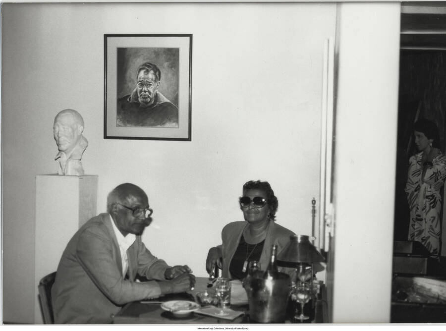 5 x 7 inch photograph; unidentified man and woman in a room with a painting and a bust of Duke Ellington