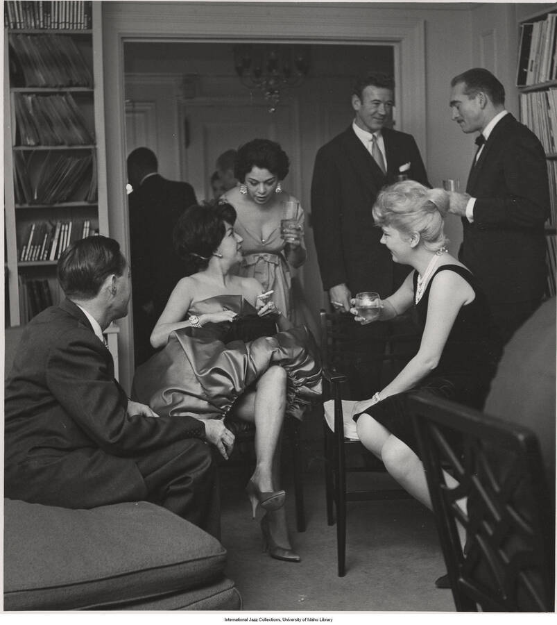 14 x 11 inch photograph; Jane and Leonard Feather with unidentified persons in a reception, probably in their apartment