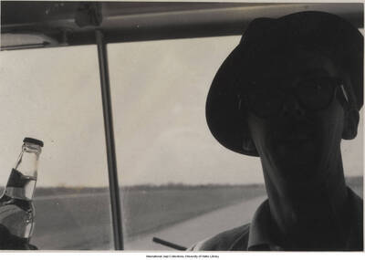 3 1/2 x 5 inch photograph; unidentified man inside a car, holding a bottle