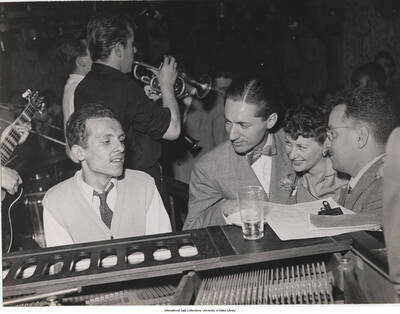 7 x 9 inch photograph; Claude Bolling and Leonard Feather accompanied by an unidentified man and a woman. Other musicians in background.