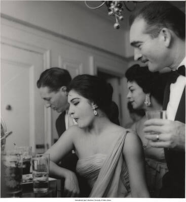 14 x 11 inch photograph; Jane and Leonard Feather with unidentified persons in a reception, probably in their apartment (1 duplicate)