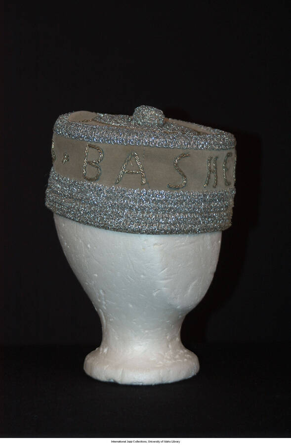 Gray, velvet, brimless fez.  Ceremonial/Masonic quality.  Silver color passmenterie embellishment around bottom of crown.  4 inch diameter circle of embellishment at center top.  1 inch pom pom at center top.  Four rosettes, flat metal beads around top center medallion, and forming words:  &quot;Bashere of Iperu&quot; around crown.  Green and white striped fabric lining.