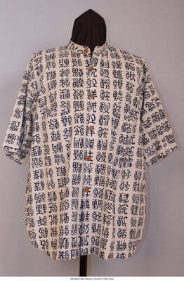 Blue/gray/white, cotton w/indigo calligraphic figures all over in rows and columns.  Indigo blue has migrated (bled) into white fabric.  Shirt tail style, short sleeves w/ standing band collar.  No labels, looks homemade.  6 brown wooden buttons center front placket.  R and L breast pockets.