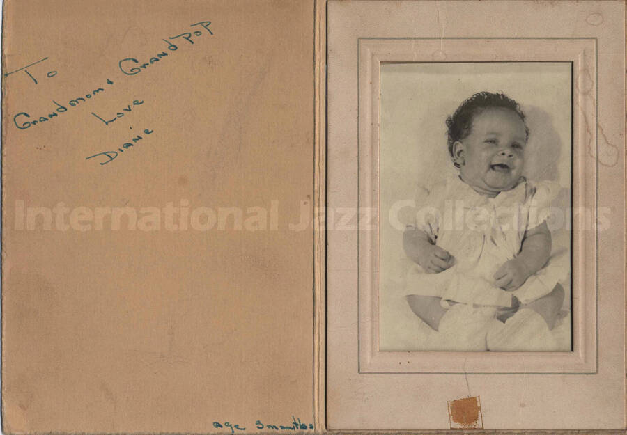 A baby. The photograph is in a paper frame dedicated to Grand mom and Grand pop by Diane, age 3 months