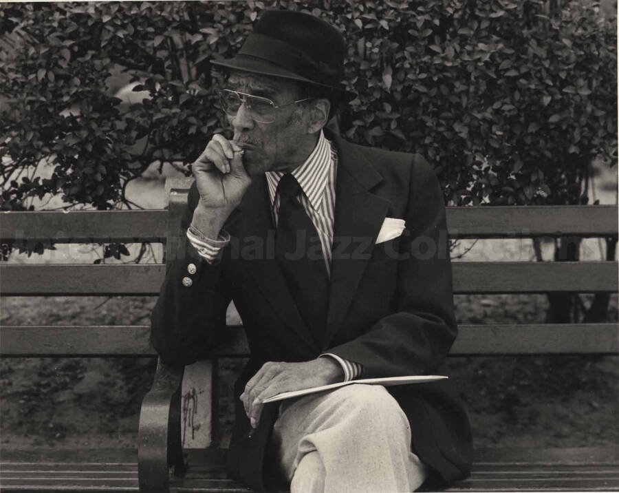 A man smoking a cigarette sitting on a park bench. Handwritten on the back of the photograph: Brother Wilbur