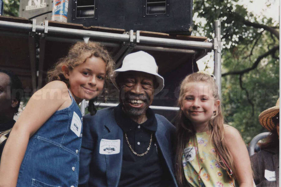 Al Grey posing with two unidentified girls at the Sixth Annual Charlie Parker Jazz Festival