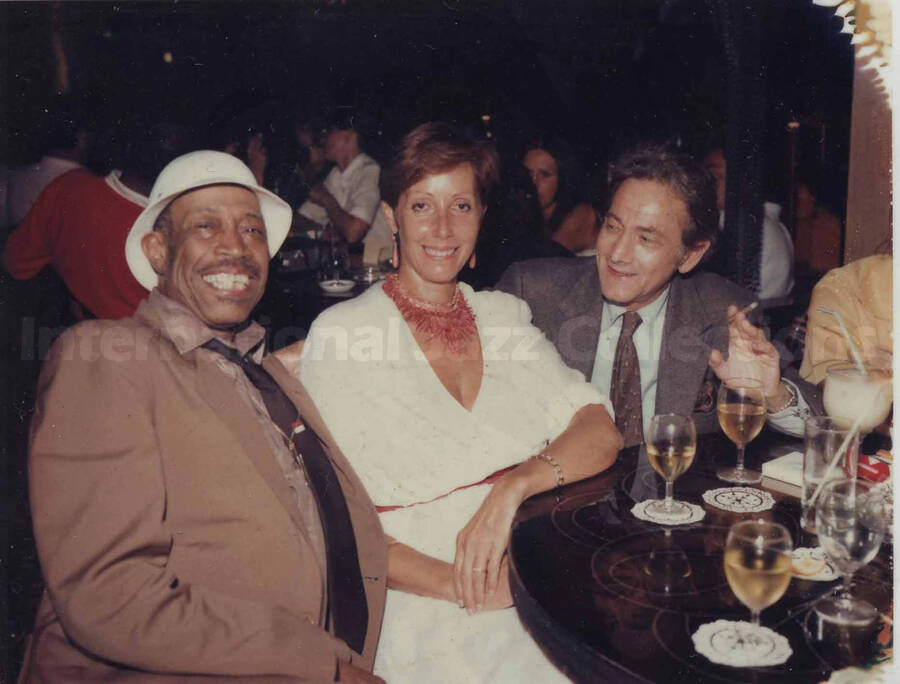 Al Grey posing with unidentified man and woman at a restaurant. The photograph is in a paper frame dedicated to "my Ace man" from [J. B. [?] and Alicia
