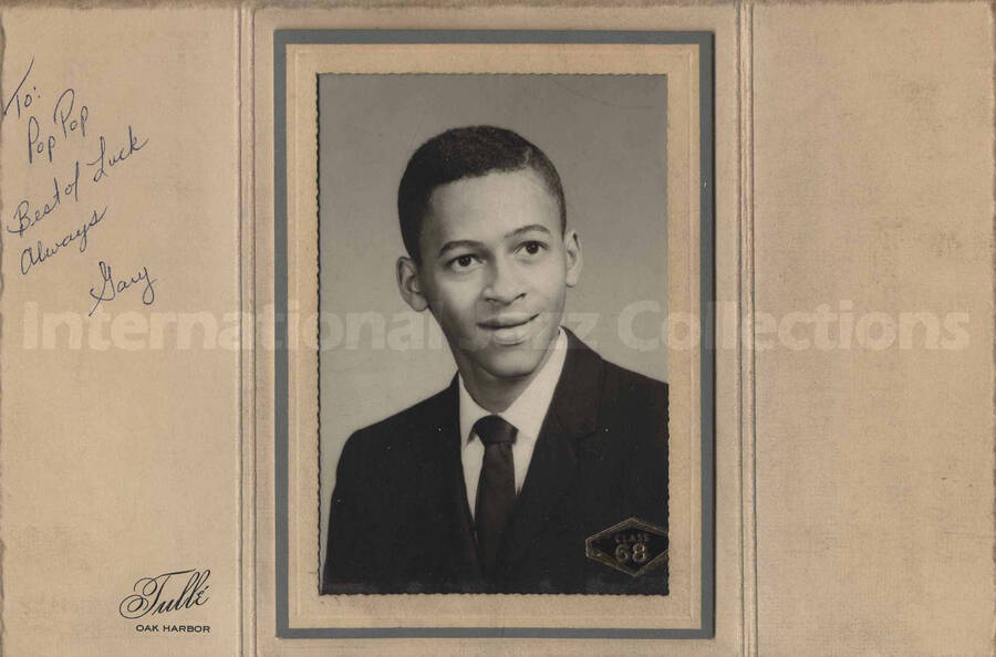 A young man. On the right bottom of the photograph there is a sticker that reads: class 68. This photograph is in a paper frame and is dedicated to Pop Pop by Gary. No inscriptions on the back of the photograph