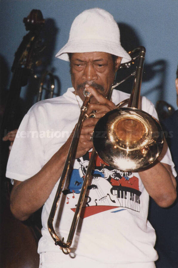 Al Grey playing the trombone. A label on the back of the photograph reads: Sunday 1991-05-31 (ear=Red Holloway);  Jazz Inn Party. Hotel "Huis ter Duin" - Noordwijk at Sea/ The Netherlands