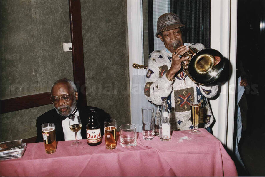 Al Grey playing the trombone next to an unidentified man at a tavern. A label on the back of the photograph reads: Sunday 1992-11-01. Jazz Mecca 1992/Maastricht-The Netherlands; Golden Tulip/Barbizon Hotel-Maastricht