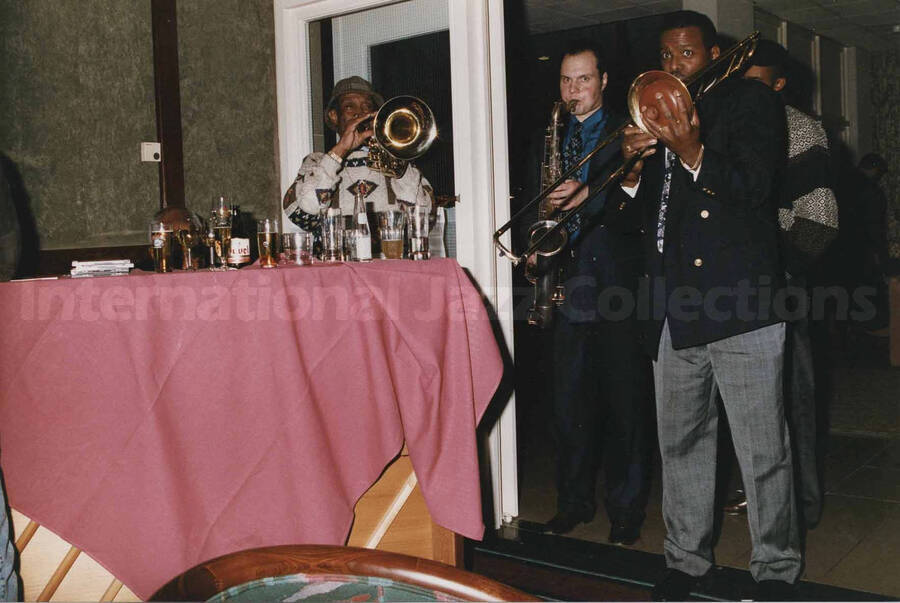 Al Grey playing the trombone alongside two unidentified musicians, one a saxophonist and the other a trombonist at a tavern. A label on the back of the photograph reads: Sunday 1992-11-01. Jazz Mecca 1992/Maastricht-The Netherlands; Golden Tulip/Barbizon Hotel-Maastricht