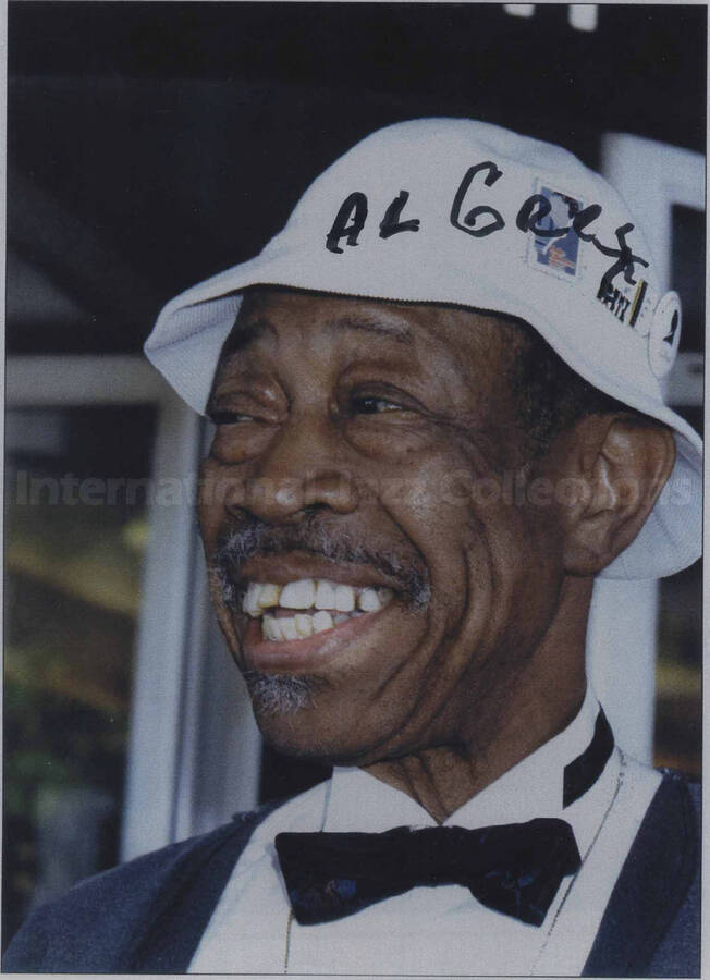 Al Grey. The photograph is under glass in an 18 x 10 1/2 frame with easel. This is a color photocopy of the photograph. There are two handwritten labels on the back of the frame. One label reads:  Taken at the North Sea Jazz Festival, 1994, by Louis Hento from "Jazz" magazine. The other label bears a dedication to Al Grey from Brian Goggin