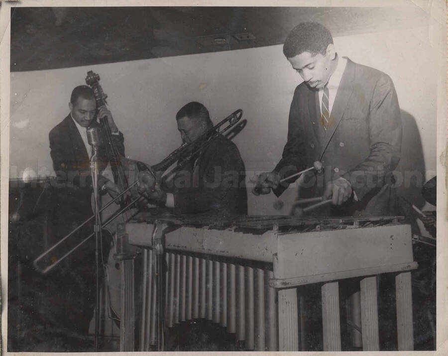 Al Grey performing with two unidentified musicians, one a bassist and the other a vibist. This photograph is pasted on a photo album