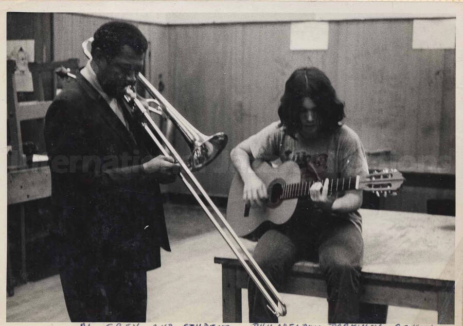 Al Grey playing the trombone with unidentified student, who is playing the guitar, at the Philadelphia Parkway School. This photograph is pasted on a photo album sheet.