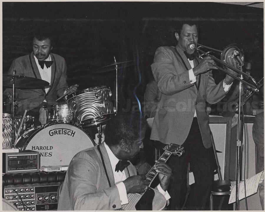 Al Grey performing in an orchestra, with drummer Harold Jones and guitarist Freddie Green. This photograph is pasted on a photo album