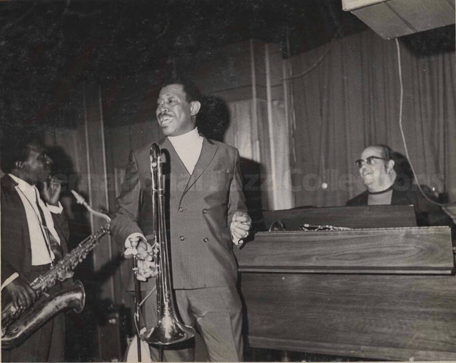 Al Grey and two unidentified musicians, one a pianist and the other a saxophonist. This photograph is pasted on a photo album