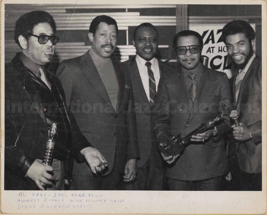 Al Grey, Dizzy Gillespie, and three unidentified men at the Jazz Club Philadelphia Awards Dinner. Gillespie and one of the men are holding trophies. This photograph is pasted on a photo album