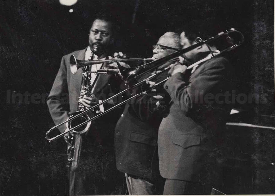 Al Grey performing with two unidentified musicians, one a trumpeter and the other a saxophonist. This photograph is pasted on a photo album