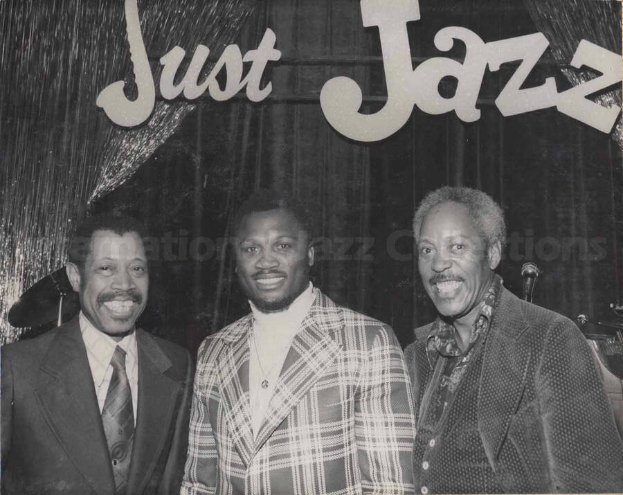 Al Grey posing with two unidentified men. On the background wall the words: Just Jazz. This photograph is pasted on a photo album