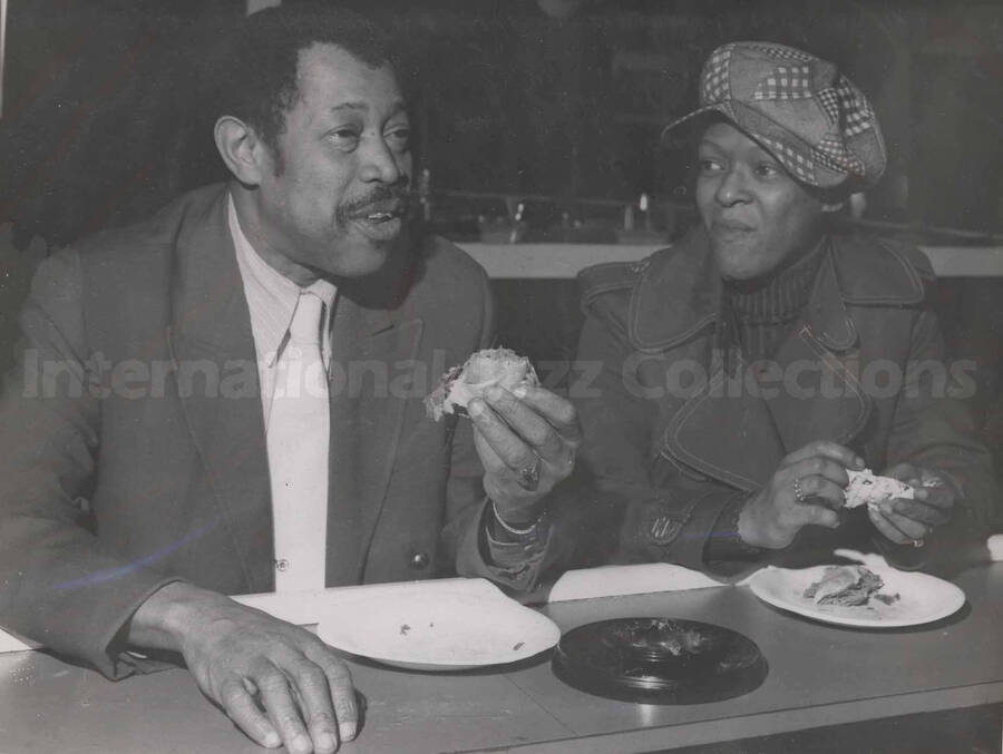 Al Grey and an unidentified woman at the counter of a tavern having a bite to eat. This photograph is pasted on a photo album