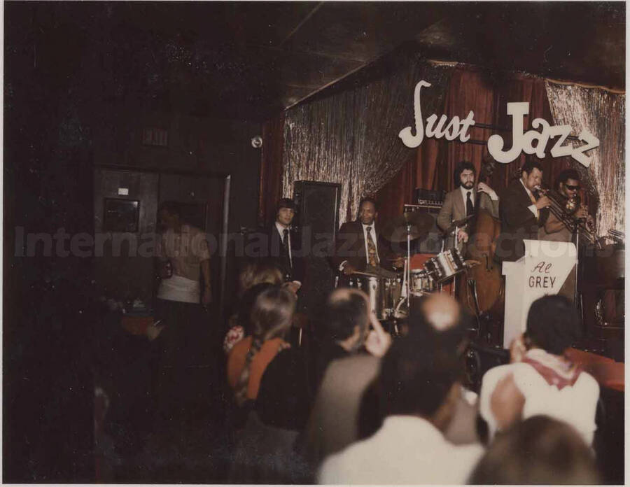 Photograph is mounted on a paper frame from "Just Jazz," Philadelphia, PA. Al Grey performing with unidentified musicians. Written on the background wall: Just Jazz. This photograph is pasted on a photo album