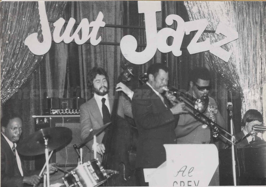 Al Grey performing with unidentified musicians. Written on the background wall: Just Jazz. This photograph is pasted on a photo album