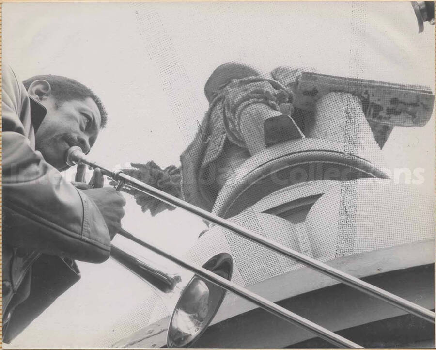 Al Grey playing the trombone at the bottom of a sculpture. This photograph is pasted on a photo album