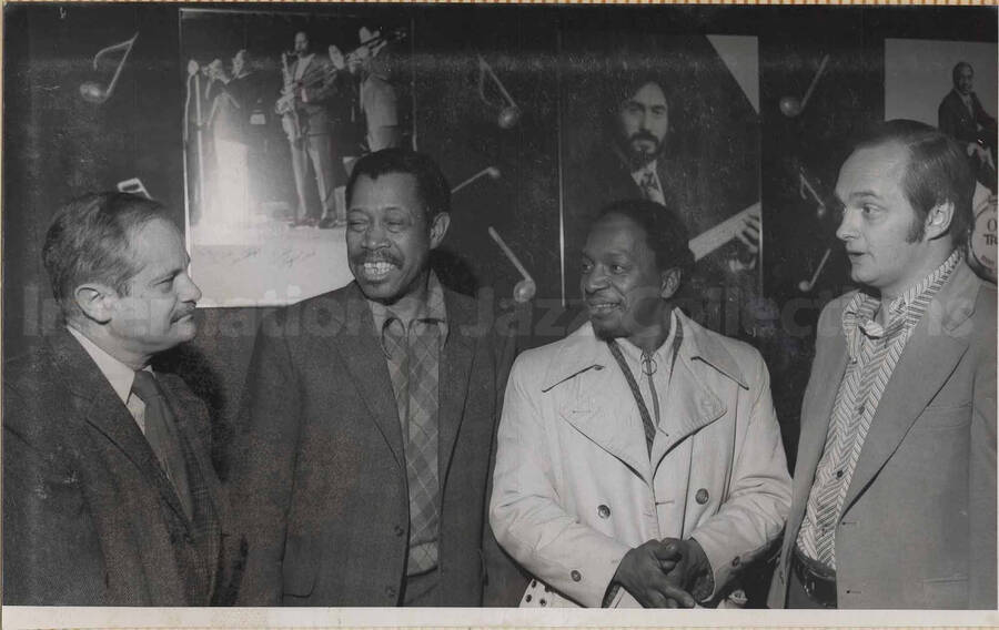 Al Grey with three unidentified men standing in front of a wall displaying some photographs.  This photograph is pasted on a photo album.