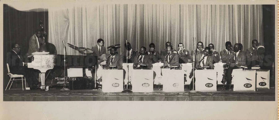 Unidentified Orchestra. Music stands in front of the musicians bear the letters "CB". This photograph is pasted on a photo album sheet.