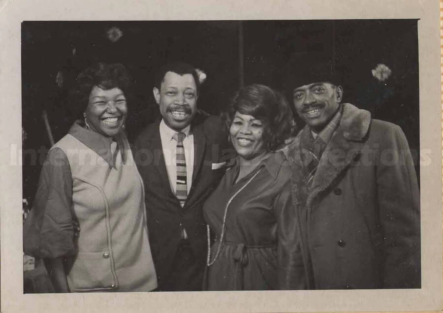 Al Grey posing with two unidentified women and an unidentified man. This photograph is pasted on a photo album sheet.