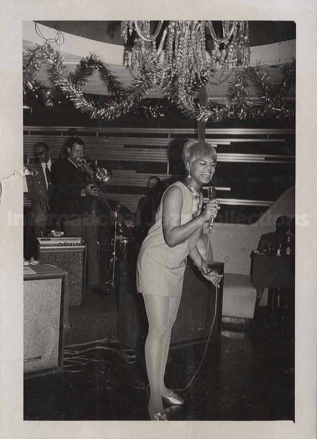 Al Grey performing with unidentified musicians and an unidentified woman singer . This photograph is pasted on a photo album sheet.