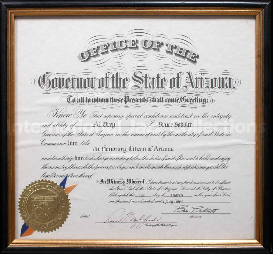 Frame holding a certificate with gold foil seal of the State of Arizona and blue and yellow ribbons under glass.  Title of Honorary Citizen of Arizona presented to Al Grey. Bruce Babbitt, Governor and Rose Mofford, Secretary of the State of Arizona. Phoenix (AZ). A label on the back of the frame reads: Berks Art, Reading (PA)