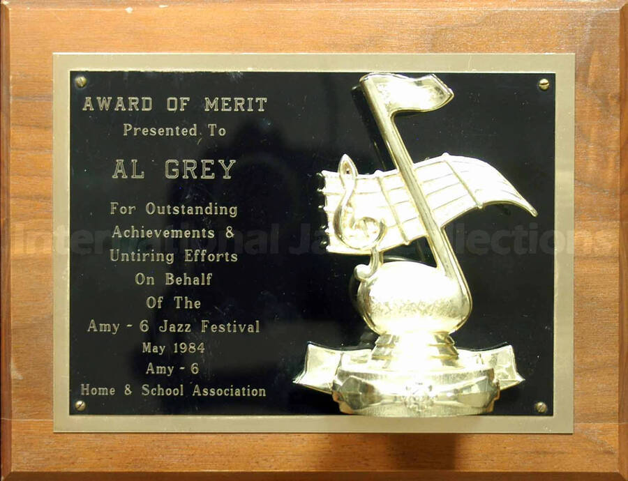 Wood finish plaque with double engraved plate bearing a musical theme. To Al Grey from the Amy-6 Home and School Association for his efforts on behalf of the Amy-6 Jazz Festival. A label on the back of the plaque reads: Spike's Trophies, a division of Gold Medal Sporting Goods