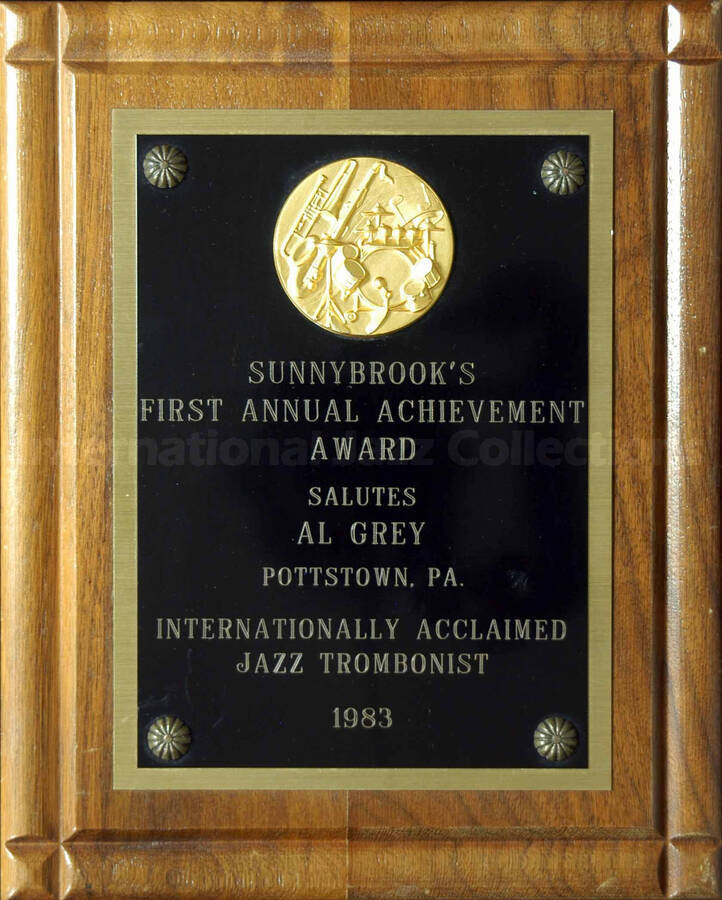 Wood finish squared border plaque with engraved double plate bearing a disk. Sunnybrook's First Annual Achievement Award presented to Al Grey, in Pottstown (PA). Stamped on the back of the plaque: Trophy & Plaque Shack, Pottstown (PA)