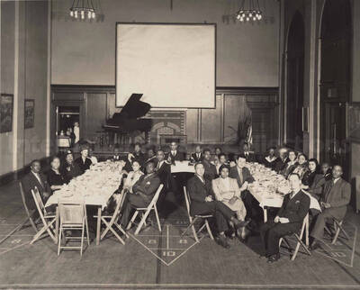 Unidentified persons sitting at a dinner table in what appears to be the gym or auditorium of a school. [Young Men's Christian Association, Pottstown, Pennsylvania]
