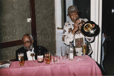 Al Grey playing the trombone next to Junior Mance at a tavern. A label on the back of the photograph reads: Sunday 1992-11-01. Jazz Mecca 1992/Maastricht-The Netherlands; Golden Tulip/Barbizon Hotel-Maastricht