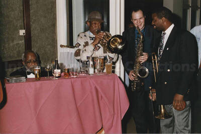 Al Grey playing the trombone alongside two unidentified musicians, one a saxophonist and the other a trombonist next to an unidentified man at a tavern. A label on the back of the photograph reads: Sunday 1992-11-01.  Jazz Mecca 1992/Maastricht-The Netherlands; Golden Tulip/Barbizon Hotel-Maastricht