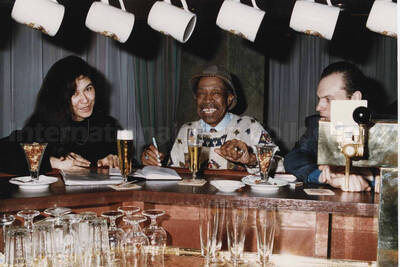 Al Grey with tenor saxophonist Dimitri Shapko and an unidentified woman at the counter of a bar. A label on the back of the photograph reads: Sunday 1992-11-01. Jazz Mecca 1992/Maastricht-The Netherlands; Golden Tulip/Barbizon Hotel-Maastricht