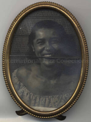 Portrait of an unidentified woman. The photograph has a signed dedication from [?]. The photograph is under glass in a 5 1/4 x 4 inch oval mettalic desk frame. No inscriptions on the back of the photograph