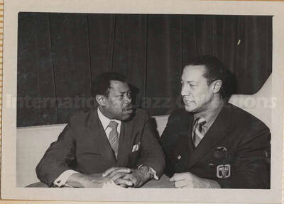 Al Grey conversing with an unidentified man. This photograph is pasted on a photo album sheet.