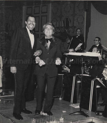 Al Grey posing with an unidentified man at the inaugural ball of the Pennsylvania Governor Milton Shapp. This photograph is pasted on a photo album