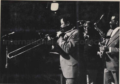 Al Grey performing with two unidentified musicians, one a trumpeter and the other a saxophonist. This photograph is pasted on a photo album