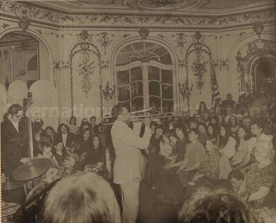 Al Grey and unidentified band performing for an audience comprised mostly of youths in a saloon decorated with musical motifs. This photograph is pasted on a photo album