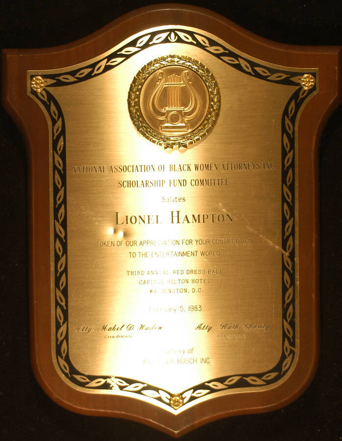 Plaque. 12 1/2"x10" Shield wood finish plaque with engraved plate bearing a disc To Lionel Hampton from the National Association of Black Women Attorneys  Scholarship Fund Committee for his contribution to the entertainment world, on the occasion of the Third Annual Red Dress Ball, at the Capitol Hilton Hotel. Mabel D. Haden, Chairman and Ruth Charity, President. Washington, D.C., Feb. 5, 1983. Courtesy of Anheuser Busch Inc.